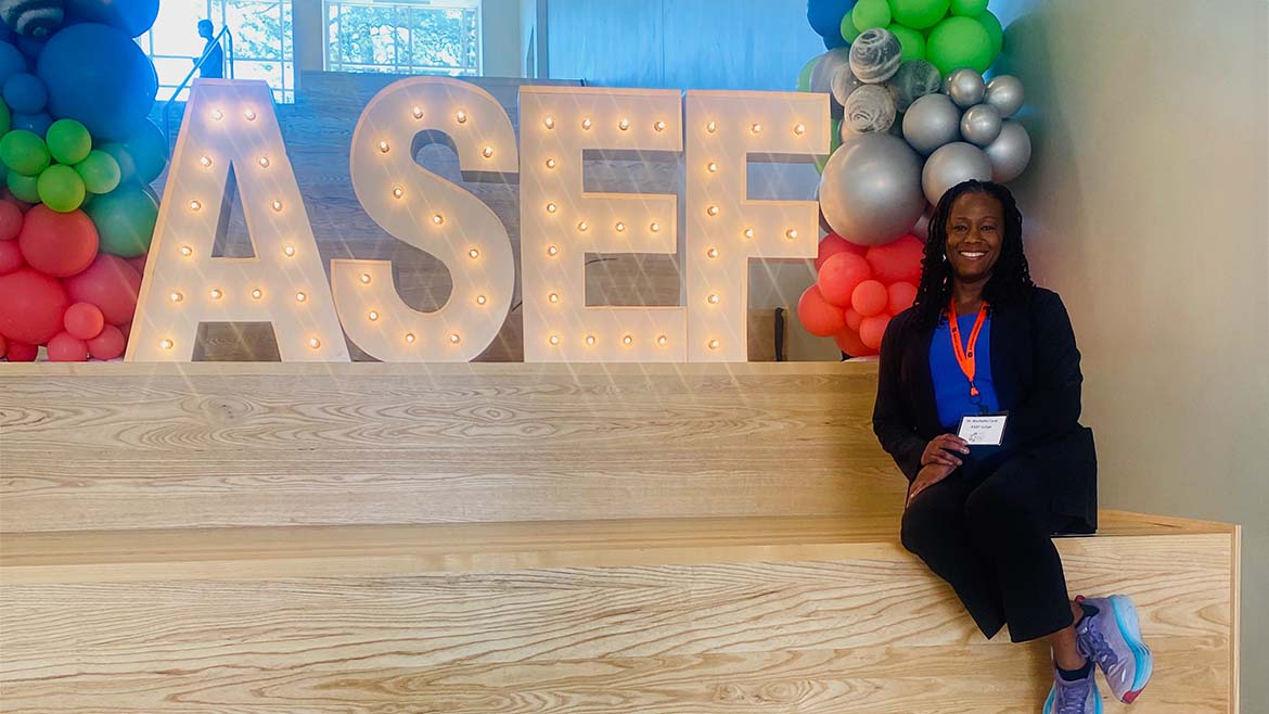 Dr. Rochelle Cook sitting beside a large ASEF sign