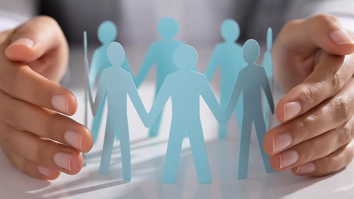 March 2024 Speaking of Quality Column feature image of person protecting circle of light blue cut out figures on a table.