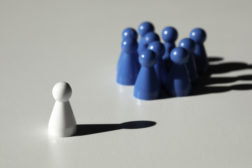 Leadership feature image of one white chess piece facing a group of blue chess pieces.