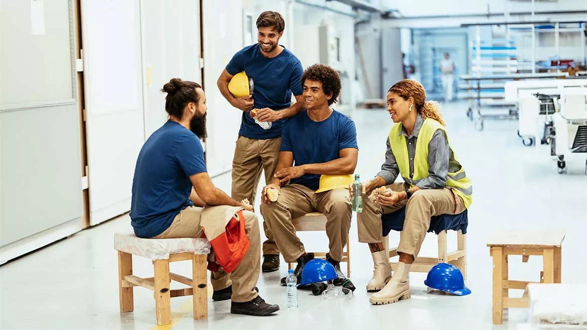 Group of workers eating and chatting, three sitting down and one standing.
