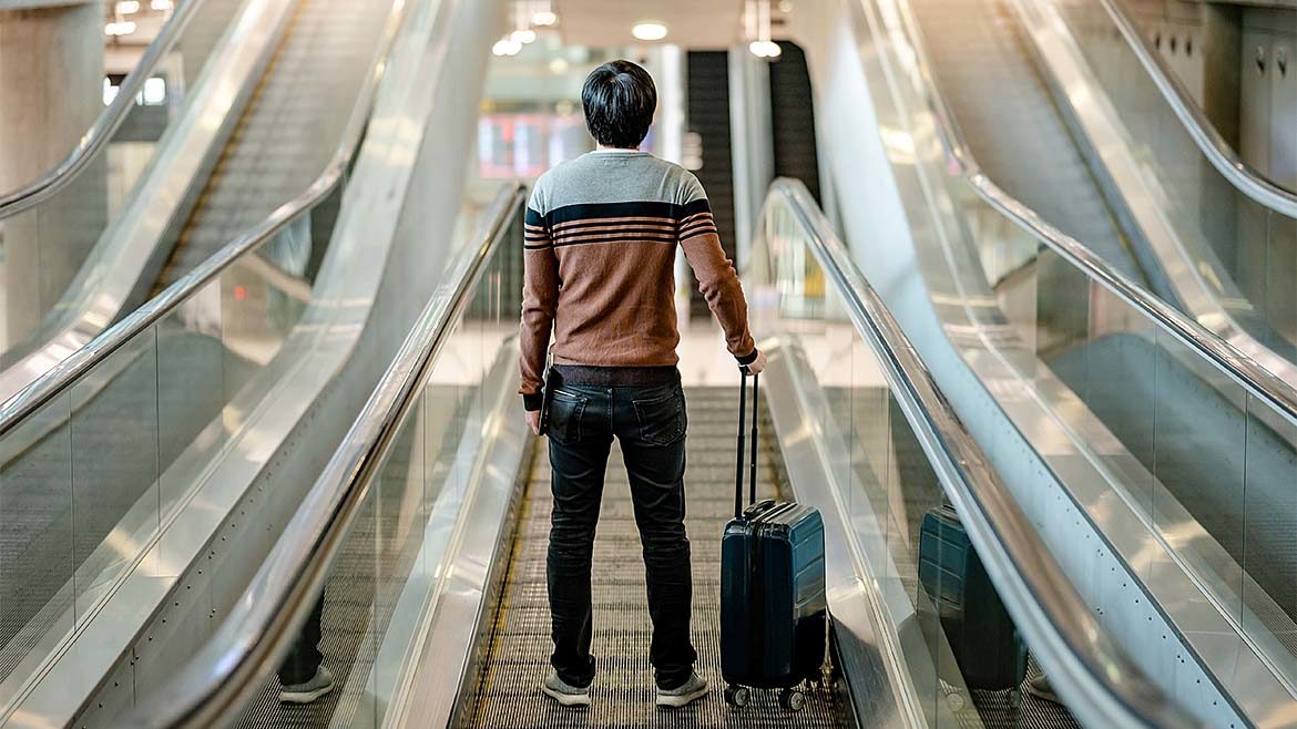 Leaning with Lazarus column feature image of tourist carrying suitcase luggage on escalator