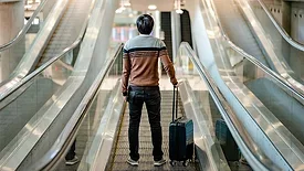 Leaning with Lazarus column feature image of tourist carrying suitcase luggage on escalator