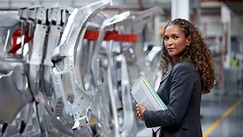 Side view of female engineer holding documents standing by car chassis in car plant.