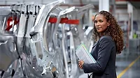 Side view of female engineer holding documents standing by car chassis in car plant.