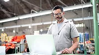 Employee working on a laptop in a factory Employee working on a laptop in a factory