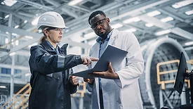 Female and male professional heavy industry engineers working in factory, using laptop.
