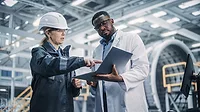 Female and male professional heavy industry engineers working in factory, using laptop.