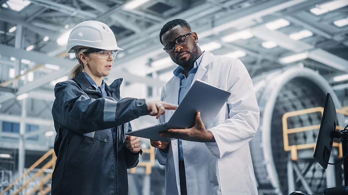 Female and male professional heavy industry engineers working in factory, using laptop.