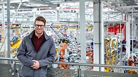 Male engineer leaning on railing in car plant.