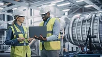 Two Professional Heavy Industry Engineers Wearing Safety Uniform and Hard Hats Working on Laptop Computer.