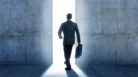 Businessman walking into bright light from inside building.