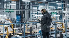 Car Factory Engineer in Work Uniform Using Tablet Computer in an Automotive Industrial Manufacturing Facility Working on Vehicle Production with Robotic Arms Technology.