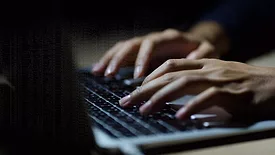 Close up of a man's hands on keyboard of lap top in the dark room.