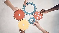 Group of five businesspeople holding and fitting gears together in an office at work. Group of five businesspeople holding and fitting gears together in an office at work. United business professionals having fun connecting gear pieces during a meeting