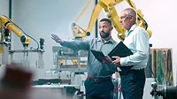 Two engineers collaborating in a warehouse Robotics and planning with two engineers collaborating in a warehouse with robotics in the background.
