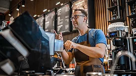 Male barista making coffee for customers at the bar.