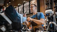 Male barista making coffee for customers at the bar.