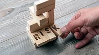Hand taking the "K" block from wooden blocks tower. Hand taking the "K" block from wooden blocks tower. The "K" is part of four long blocks that say "RISK".