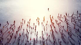 Overhead view of a community of people following a leader towards a bright light.