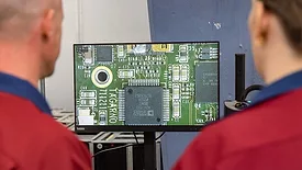 Two operators using a digital microscope to look at a magnified image of an electronics part.