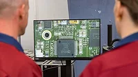 Two operators using a digital microscope to look at a magnified image of an electronics part.