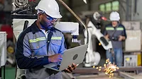 Mechanical engineer holding a laptop, doing maintenance work Mechanical engineer holding a laptop, doing maintenance work, while standing over the robotic welding machine.