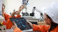 Female maintenance engineer working with a digital tablet and robotic arm in lab.