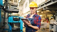 Female worker in safety gear and using a tablet in a plant.