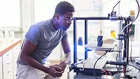 African-American male engineer using a 3D printer in the laboratory while studying a product prototype, and technology.