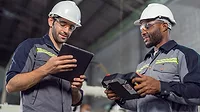 Two Industry engineers stand and discuss work in the factory workshop.