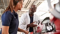 Engineer talking to female apprentice by machinery, close up.