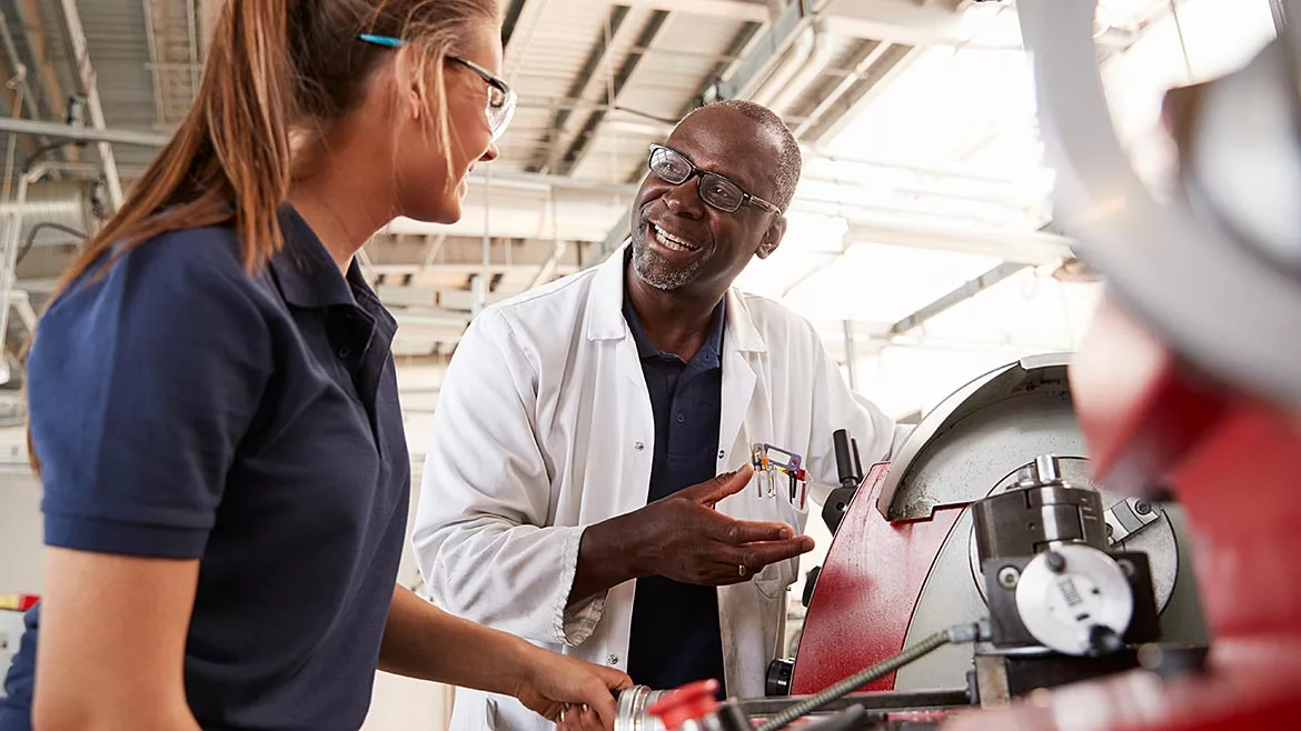 Engineer talking to female apprentice by machinery, close up.