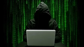 Hacker in a dark hoodie committing cyber crime with a laptop, green binary numbers on a black background.