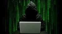 Hacker in a dark hoodie committing cyber crime with a laptop, green binary numbers on a black background.