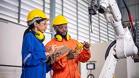 Female engineer and a male technician investigate the problem of the operation of the robot arm in the factory.