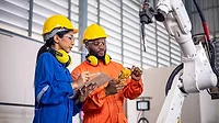 Female engineer and a male technician investigate the problem of the operation of the robot arm in the factory.