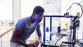 African-American designer or engineer using a 3D printer in the laboratory while studying a product prototype, and technology.