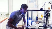 African-American designer or engineer using a 3D printer in the laboratory while studying a product prototype, and technology.