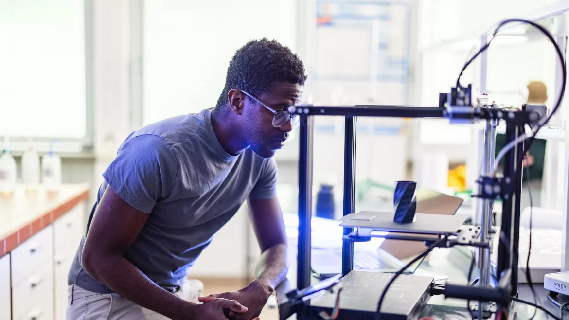 African-American designer or engineer using a 3D printer in the laboratory while studying a product prototype, and technology.
