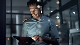 A businessman working in the dark on a tablet with a blurred background.