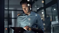 A businessman working in the dark on a tablet with a blurred background.