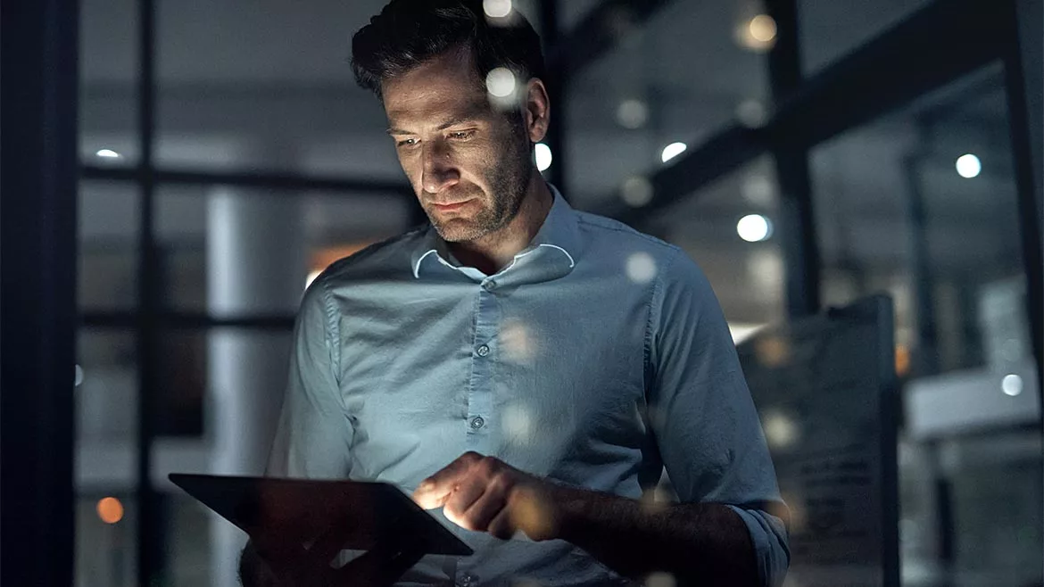 A businessman working in the dark on a tablet with a blurred background.