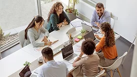 Conference room meeting with a diverse group of people, using laptops and one tablet.