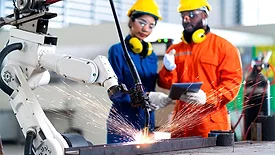 Male and female technicians using a tablet and watching a robot arm system welding.