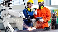 Male and female technicians watching a robot arm welding Male and female technicians using a tablet and watching a robot arm system welding.
