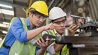 Two professional technicians working in an industrial plant, one holding a tablet.
