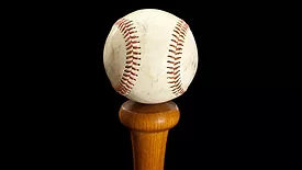 Baseball sitting on top of a bat handle with a black background.