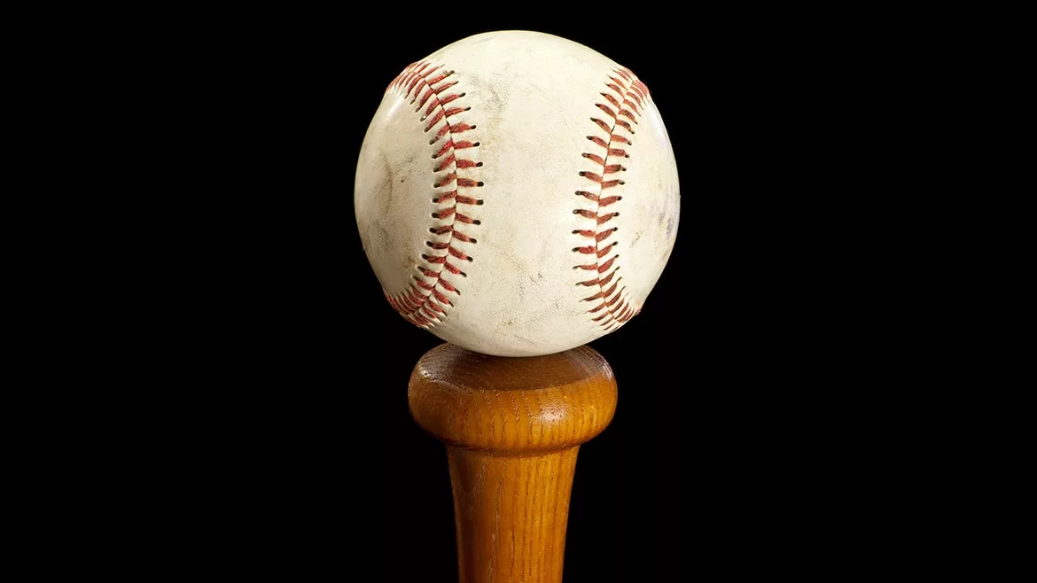 Baseball sitting on top of a bat handle with a black background.
