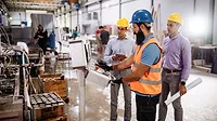 Engineers in factory hall, performing quality control. Manufacturing occupation in modern industrial hall, with automated process and robots. Metal processing industry and warehouse.