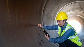 A female engineer using an instrument to measure inside a pipe.